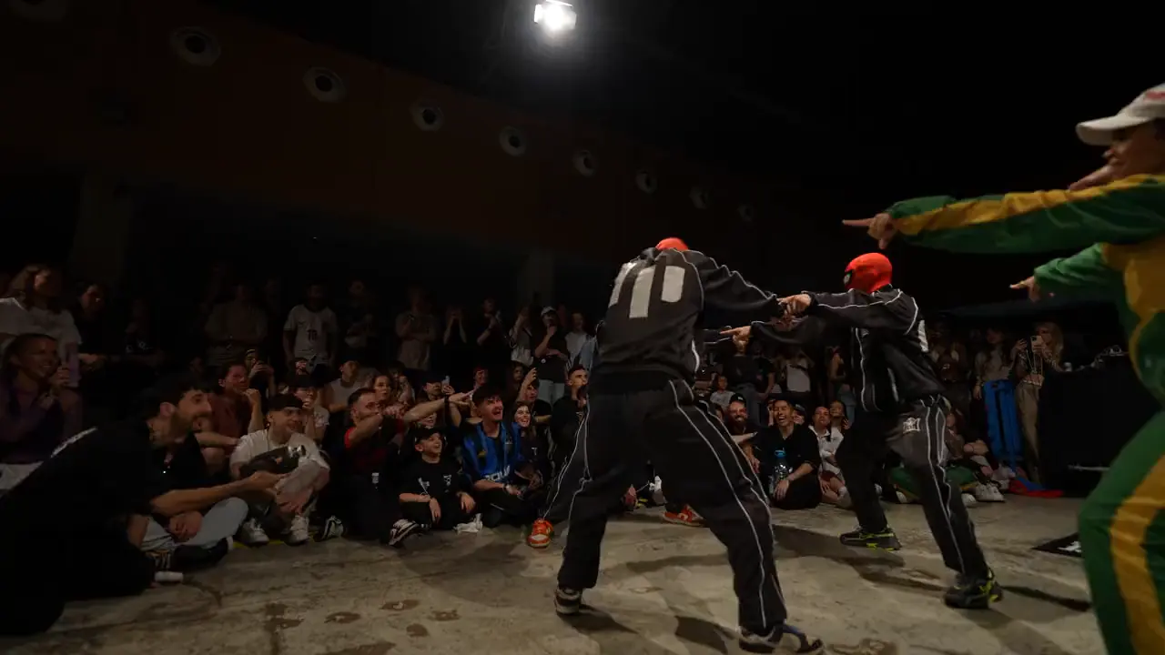 Dancers in red masks on the floor under a spotlight, facing the crowd